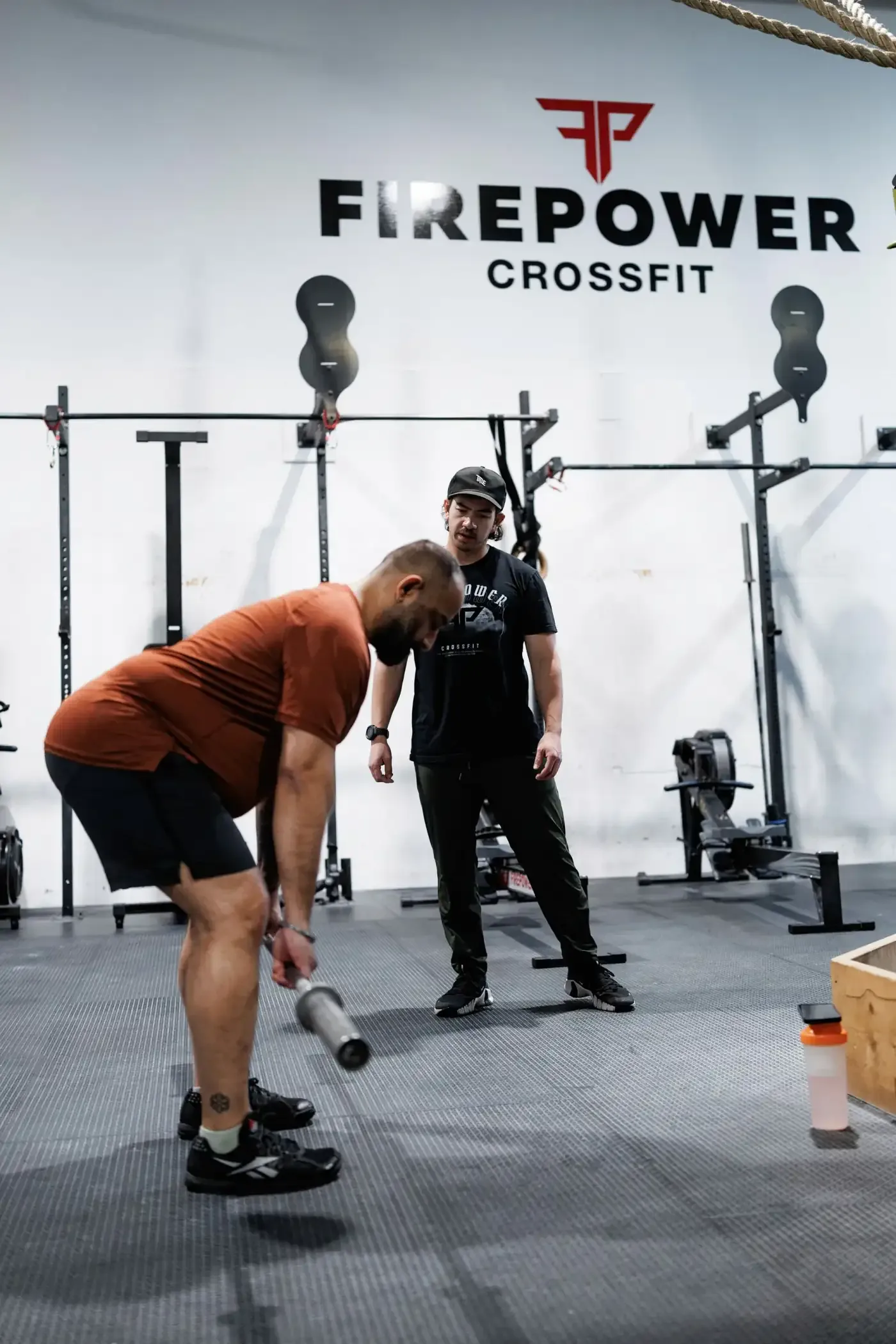 A FirePower coach guiding a member through a lift under the FirePower CrossFit wall